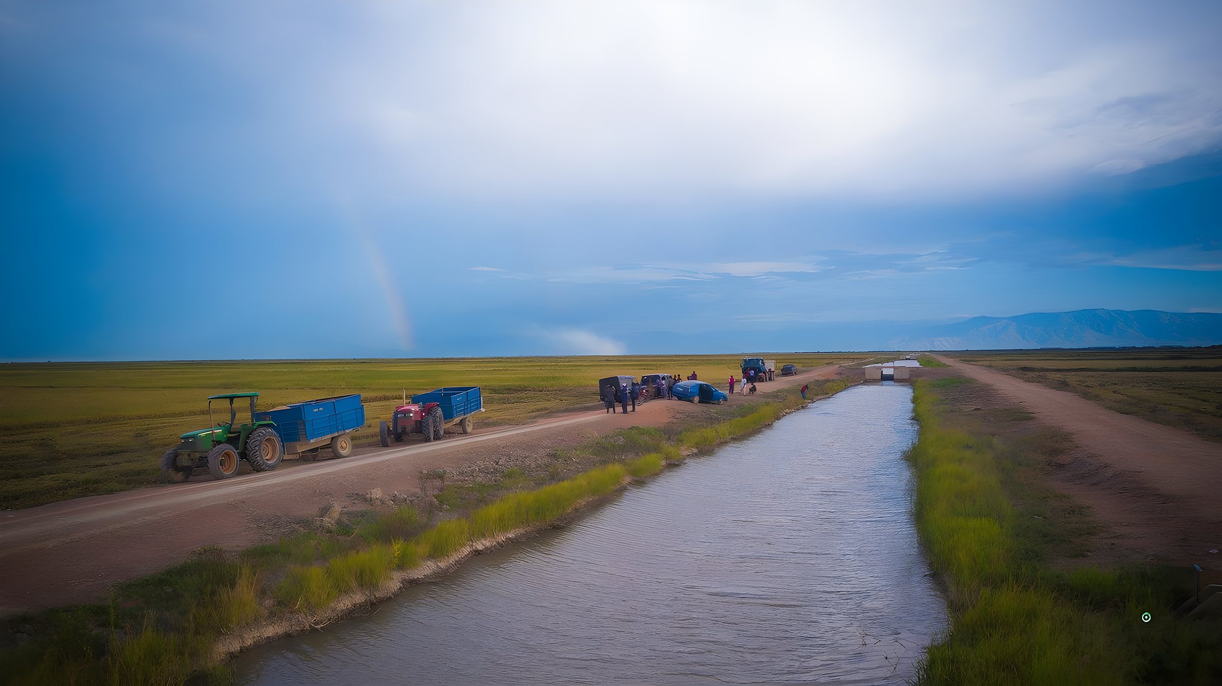 An irrigation canal through rice fields at Kapunga, with tractors and farmers at the roadside