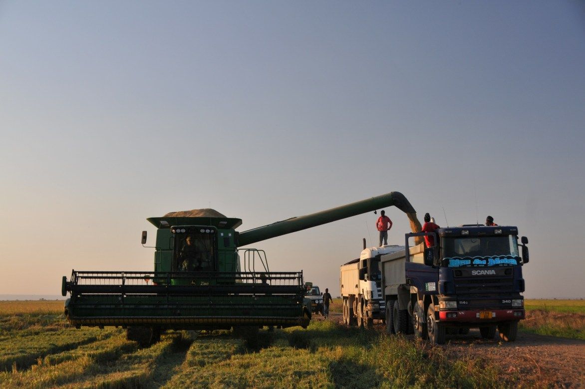 A combine harvester unloads grain into a truck at dusk