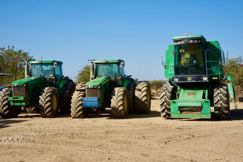 Three green John Deere tractors and a combine harvester parked in a row
